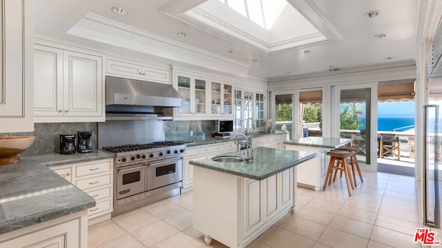 kitchen featuring an island with sink, light tile patterned floors, range with two ovens, and backsplash