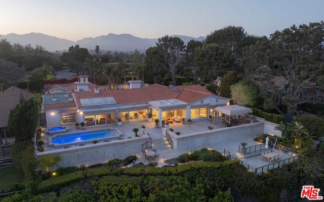 back house at dusk featuring a mountain view and a patio