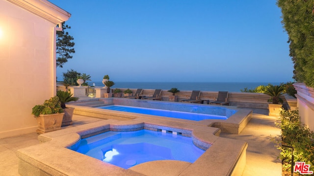 view of pool featuring an in ground hot tub, a water view, and a patio area