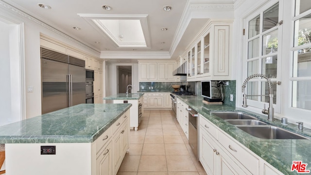 kitchen featuring sink, backsplash, light tile patterned floors, a kitchen island with sink, and built in appliances