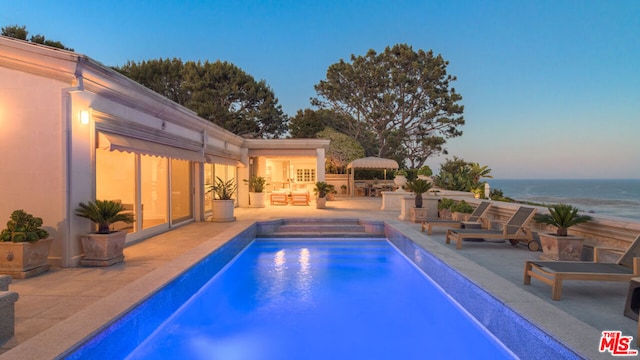 pool at dusk with a patio area, a jacuzzi, and a water view