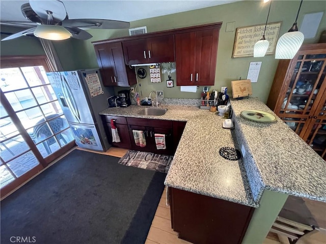 kitchen featuring stainless steel refrigerator with ice dispenser, sink, hanging light fixtures, kitchen peninsula, and ceiling fan