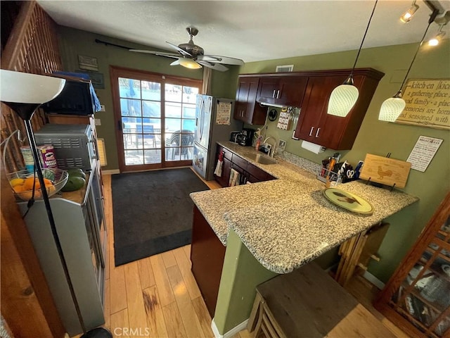 kitchen featuring a kitchen bar, light hardwood / wood-style floors, sink, decorative light fixtures, and kitchen peninsula