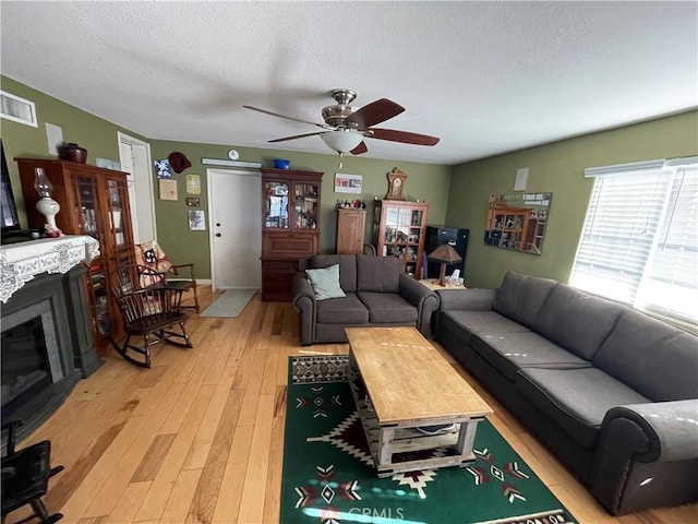 living room with ceiling fan, a textured ceiling, and light wood-type flooring