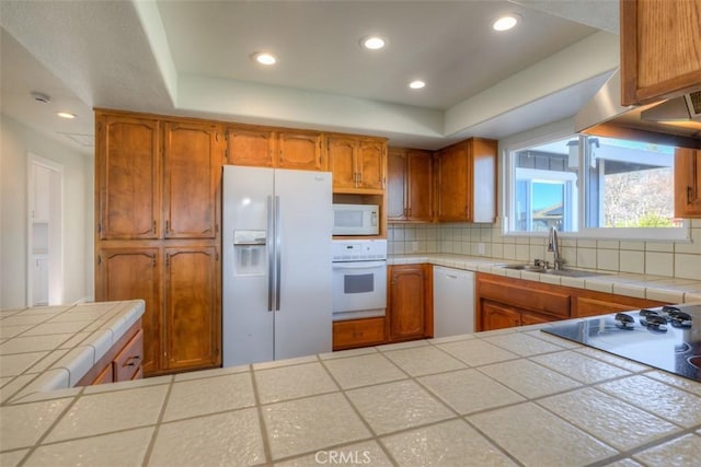 kitchen with white appliances, tile counters, decorative backsplash, sink, and a tray ceiling