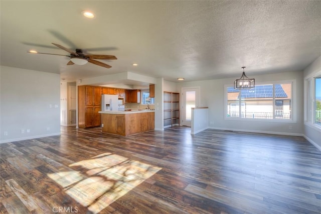 unfurnished living room with sink, dark wood-type flooring, and ceiling fan with notable chandelier