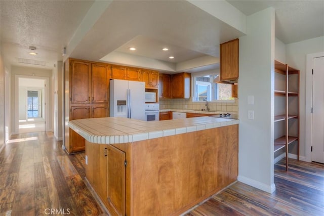 kitchen featuring white appliances, kitchen peninsula, plenty of natural light, and tile countertops