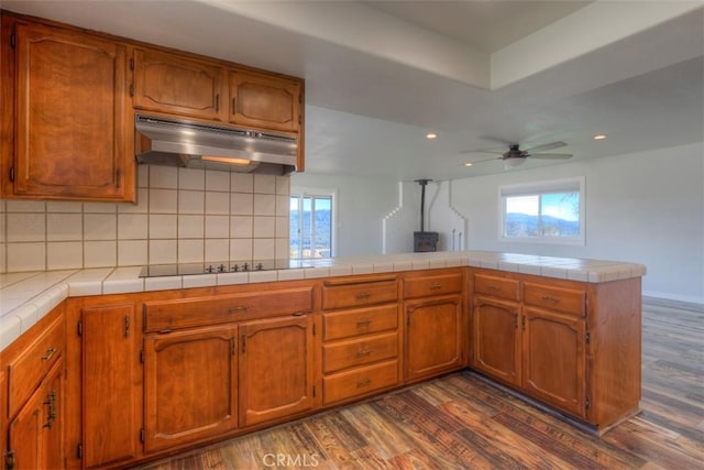 kitchen featuring dark wood-type flooring, black electric stovetop, backsplash, kitchen peninsula, and tile countertops