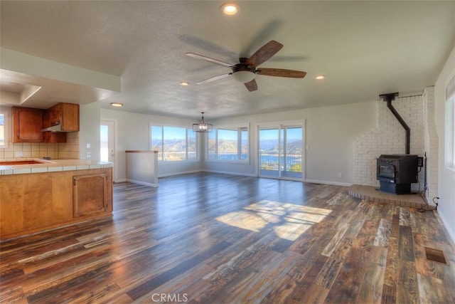 unfurnished living room with a wood stove, ceiling fan, and dark hardwood / wood-style flooring