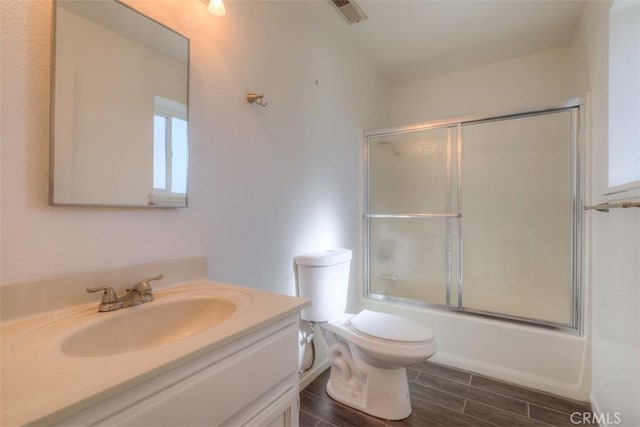 bathroom featuring toilet, vanity, visible vents, bath / shower combo with glass door, and wood finish floors