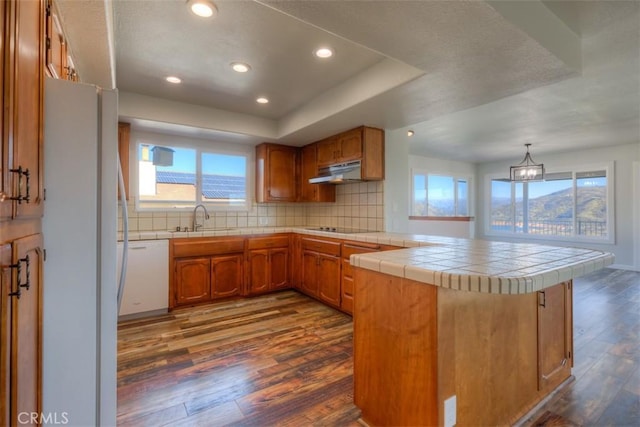 kitchen with brown cabinets, white appliances, dark wood-style floors, and a peninsula
