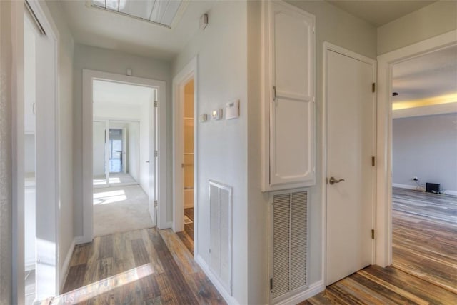 corridor featuring baseboards, visible vents, attic access, and wood finished floors