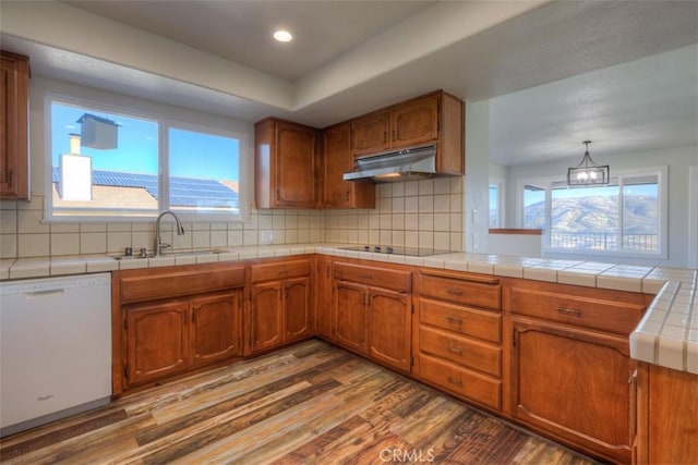 kitchen with a sink, under cabinet range hood, white dishwasher, brown cabinetry, and wood finished floors