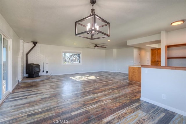 unfurnished living room featuring dark wood-type flooring, a wood stove, and ceiling fan with notable chandelier