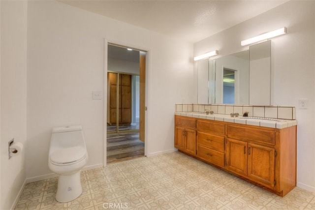 bathroom featuring double vanity, a sink, toilet, and baseboards
