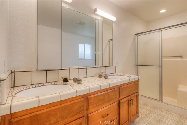 bathroom featuring a shower stall, a sink, double vanity, recessed lighting, and tile patterned floors