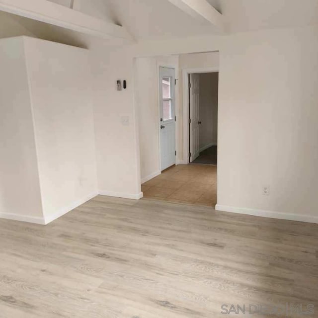 empty room featuring light hardwood / wood-style floors and lofted ceiling with beams