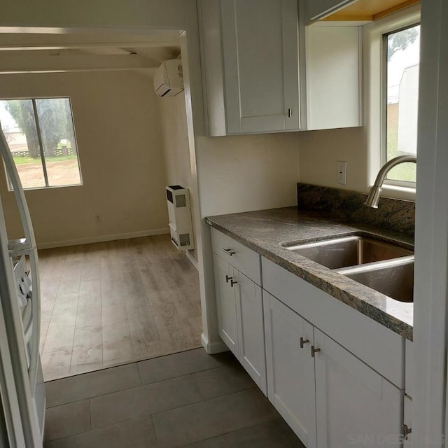 kitchen with white cabinetry, dark stone counters, sink, a wall mounted AC, and light tile patterned floors