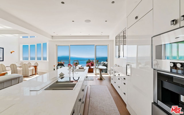 kitchen featuring hardwood / wood-style flooring, a water view, a healthy amount of sunlight, and white cabinetry