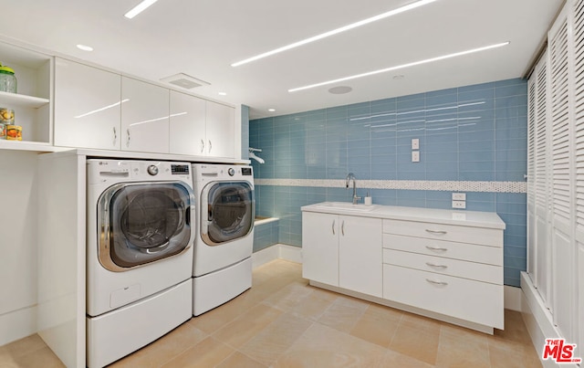 laundry area featuring tile walls, sink, light tile patterned floors, washer and dryer, and cabinets