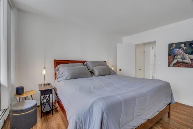 bedroom with hardwood / wood-style floors and a baseboard heating unit