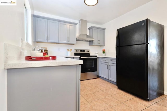 kitchen with wall chimney exhaust hood, black fridge, stainless steel electric range oven, and light tile patterned floors