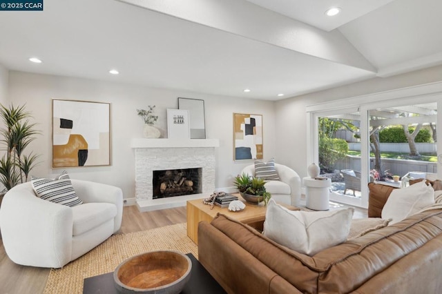 living room with vaulted ceiling, a stone fireplace, and light hardwood / wood-style floors