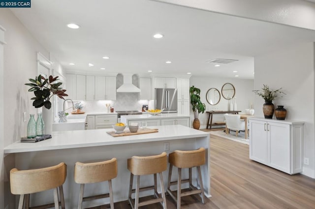 kitchen with white cabinetry, wall chimney exhaust hood, stainless steel appliances, and a breakfast bar