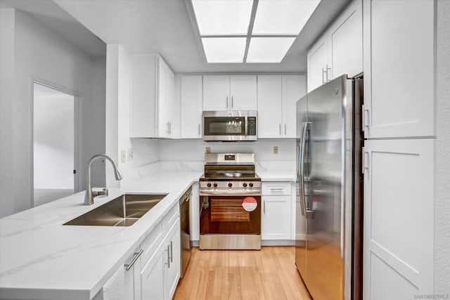 kitchen featuring light stone countertops, white cabinetry, stainless steel appliances, light hardwood / wood-style floors, and sink