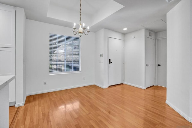 unfurnished dining area featuring a tray ceiling, an inviting chandelier, and light wood-type flooring