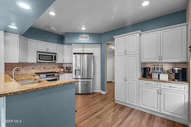 kitchen with tasteful backsplash, white cabinets, light wood-type flooring, sink, and stainless steel appliances