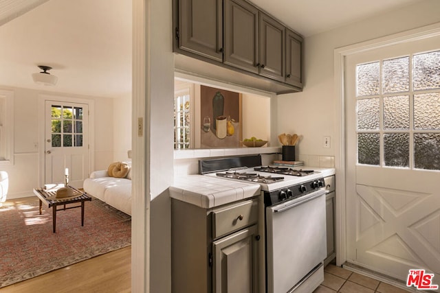 kitchen with light wood-type flooring, gas range gas stove, and tile countertops