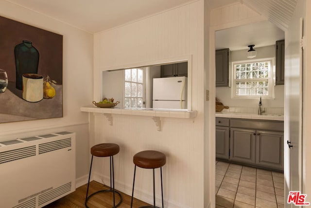 kitchen featuring sink, white refrigerator, gray cabinetry, tile countertops, and a breakfast bar area