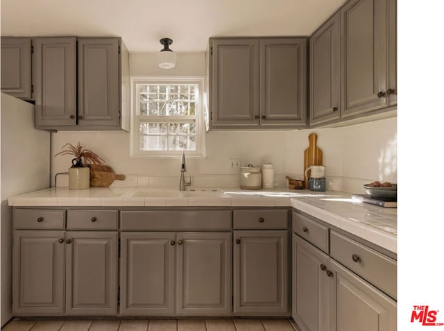 kitchen with sink, tile counters, and gray cabinetry