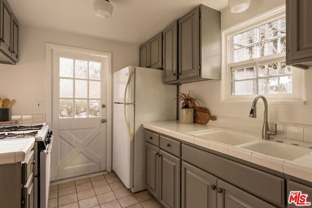 kitchen featuring sink, light tile patterned floors, tile counters, and stainless steel gas range oven