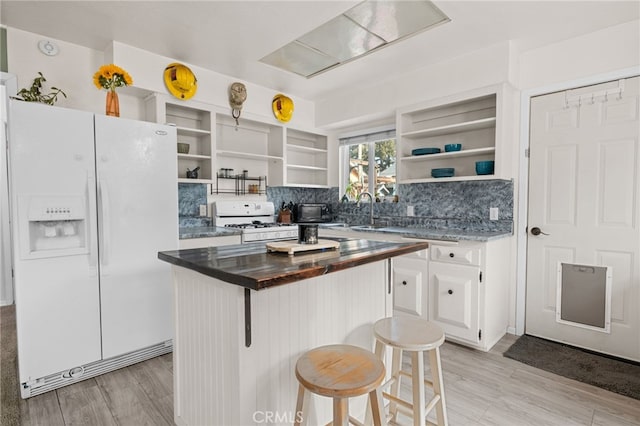 kitchen with white cabinets, a kitchen breakfast bar, a center island, light hardwood / wood-style floors, and white appliances