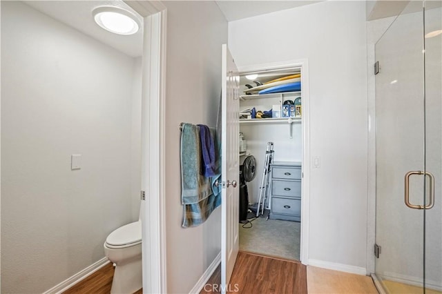 bathroom with hardwood / wood-style floors, toilet, and a shower with shower door