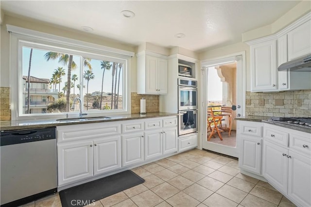 kitchen with sink, backsplash, white cabinetry, light tile patterned floors, and stainless steel appliances