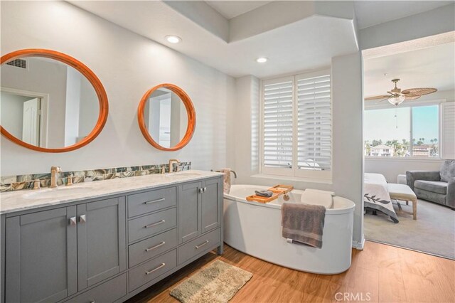 bathroom featuring ceiling fan, wood-type flooring, vanity, and a bathing tub