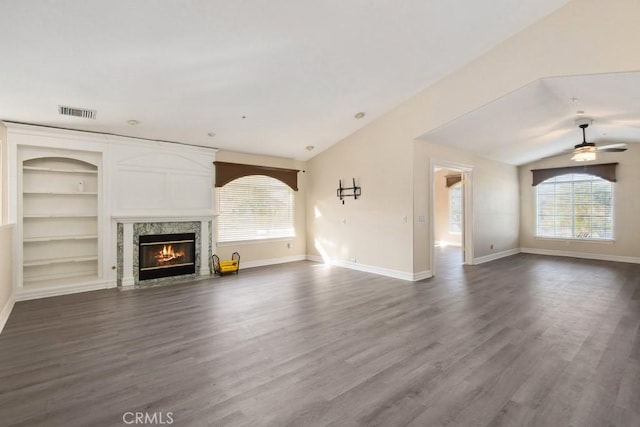 unfurnished living room featuring built in shelves, vaulted ceiling, a premium fireplace, and a healthy amount of sunlight