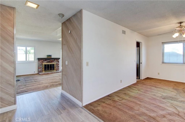 empty room with a fireplace, light hardwood / wood-style floors, a textured ceiling, and ceiling fan