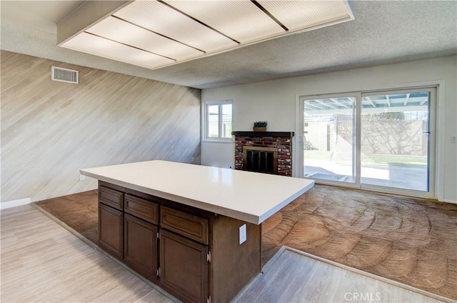 kitchen with dark brown cabinetry, light hardwood / wood-style flooring, a fireplace, and a textured ceiling