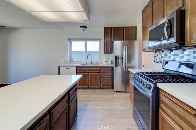 kitchen featuring sink, decorative backsplash, light hardwood / wood-style flooring, and appliances with stainless steel finishes