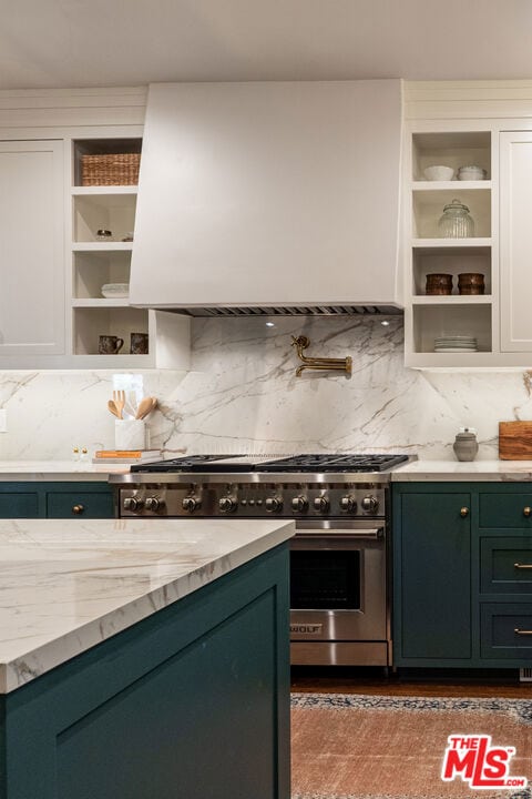 kitchen with high end stainless steel range oven, premium range hood, light stone countertops, and tasteful backsplash