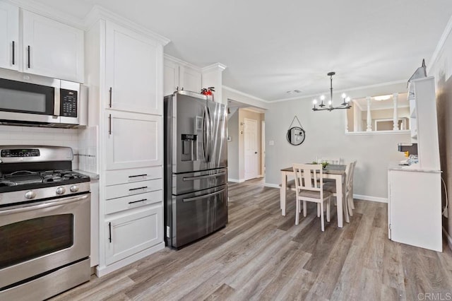 kitchen with white cabinets, stainless steel appliances, ornamental molding, a chandelier, and light wood-type flooring