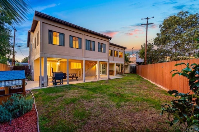 back house at dusk featuring a patio and a yard