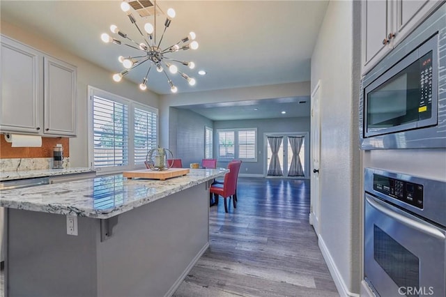 kitchen with dark wood-type flooring, a kitchen island, stainless steel appliances, light stone counters, and a kitchen bar