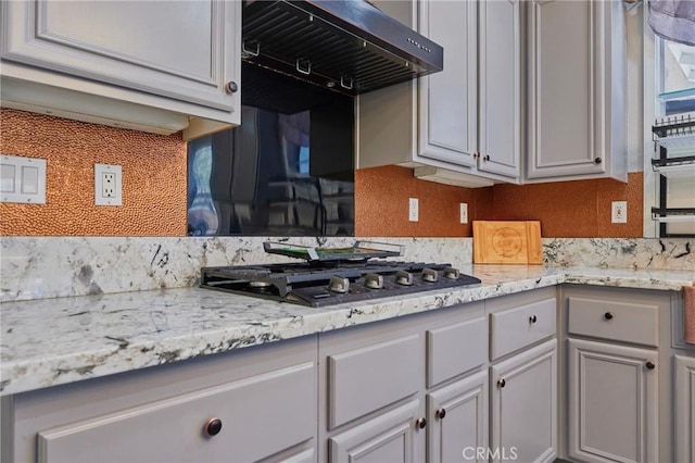 kitchen featuring wall chimney range hood, light stone countertops, and stainless steel gas stovetop