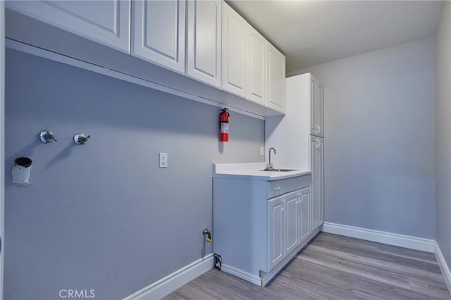 clothes washing area featuring cabinets, hookup for a gas dryer, sink, and light wood-type flooring