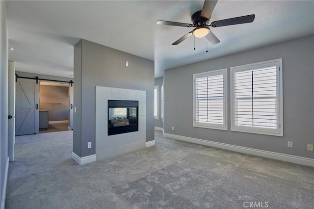 unfurnished living room featuring ceiling fan, light colored carpet, a barn door, and a tiled fireplace